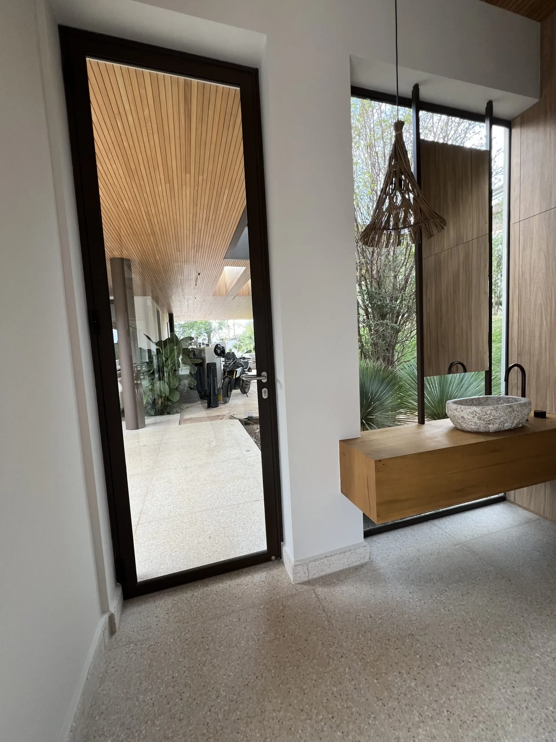 Detalhe de porta de vidro com esquadria de alumínio escuro, vista para área externa.