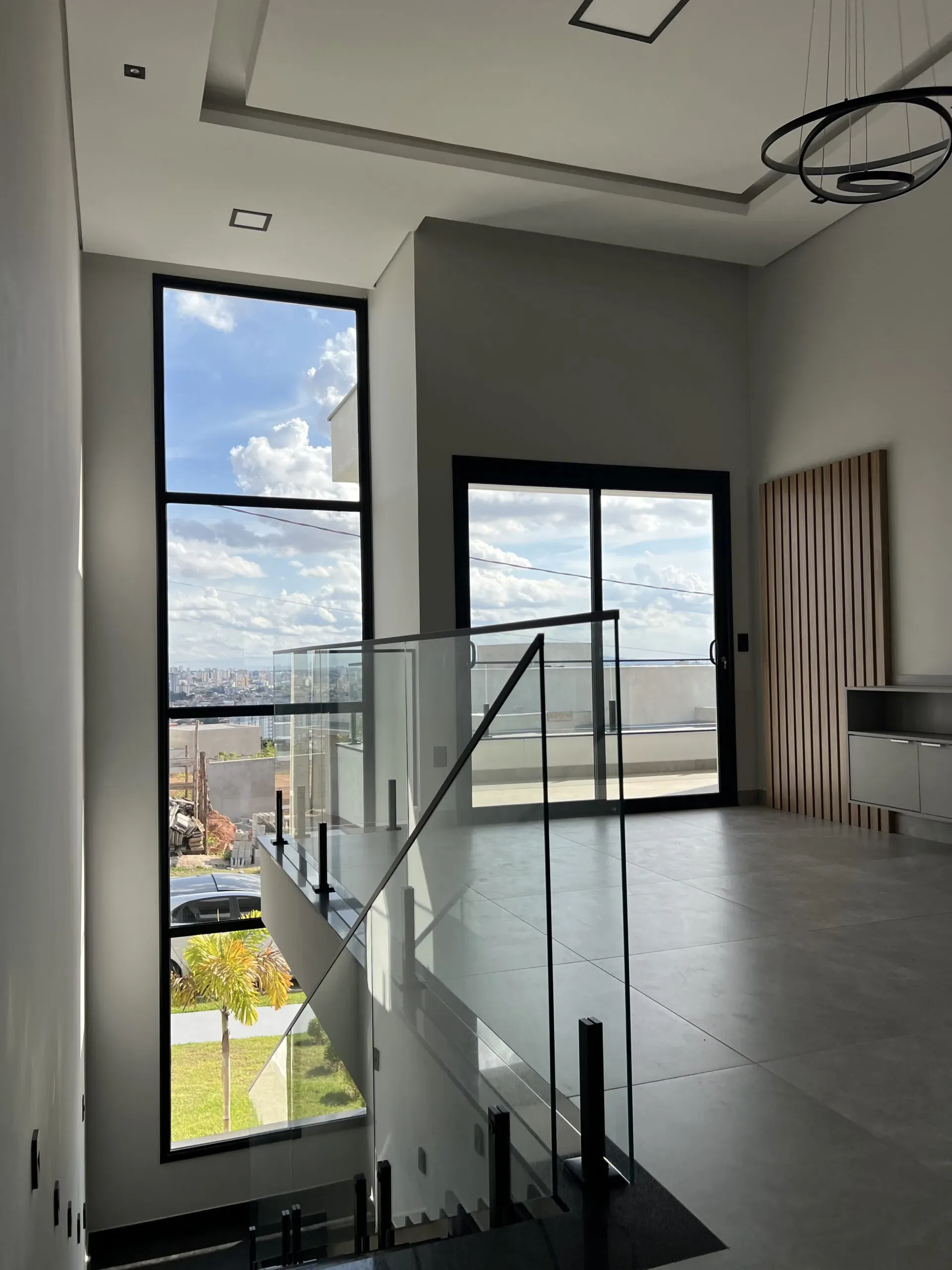 Guarda-corpo de vidro protegendo escada interna, com vista para porta de correr e janela de alumínio preto.