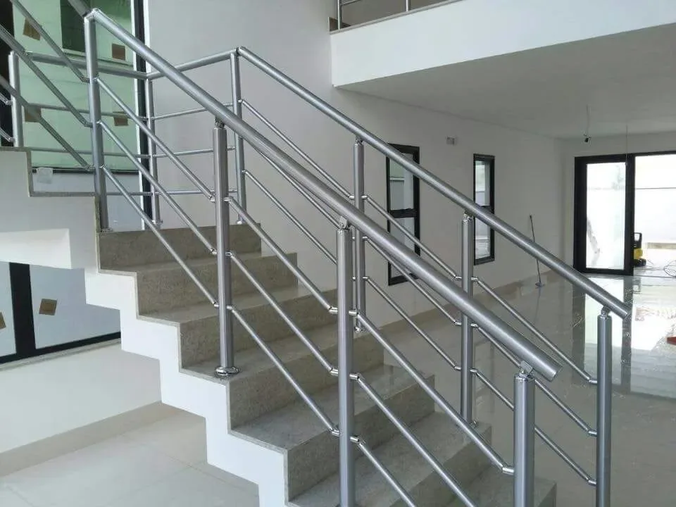 Guarda-corpo em inox escovado com tubos horizontais e montantes verticais instalado em escada interna de residência em fase final de obra.