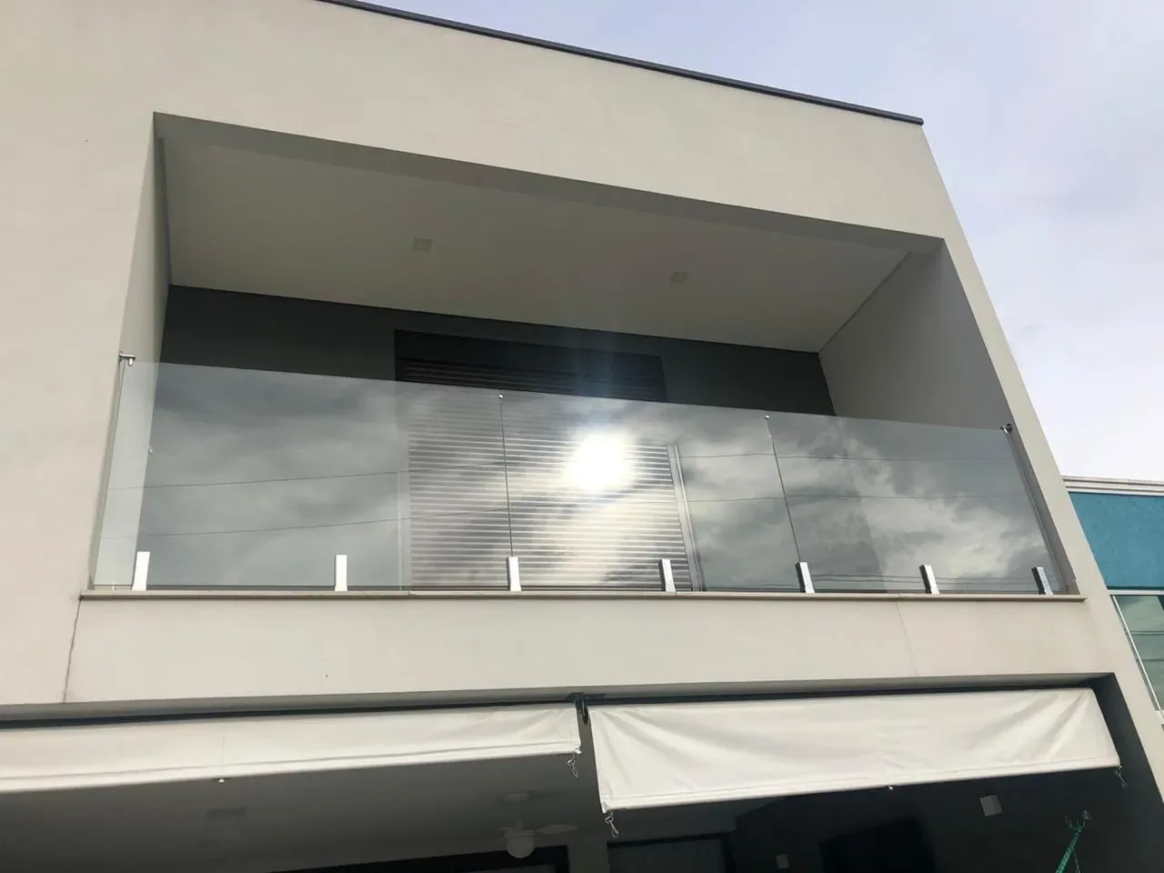 Guarda-corpo de vidro temperado fixado por ponteiras metálicas em sacada de edifício moderno com fachada em concreto aparente, visto de baixo para cima.