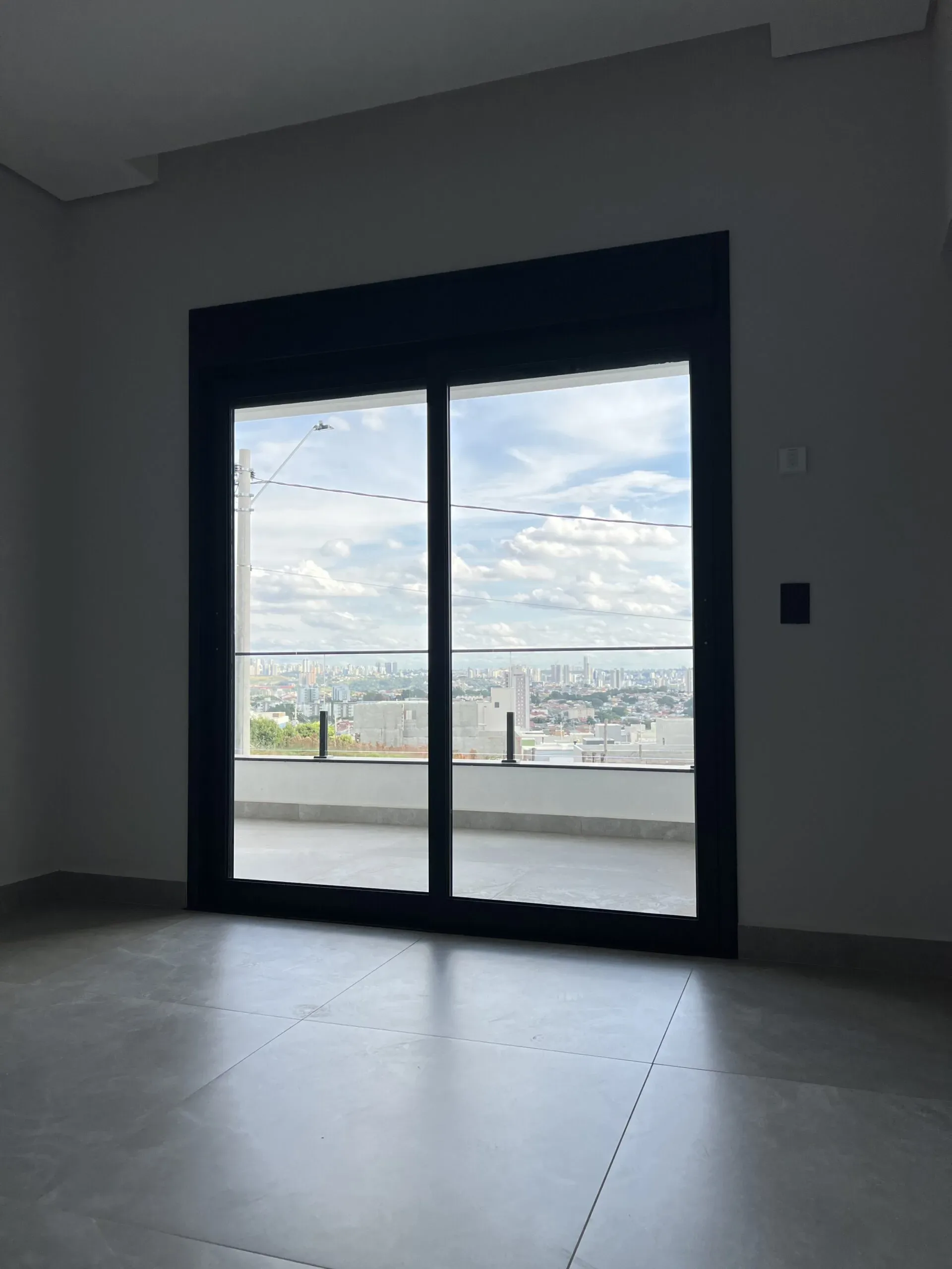 Quarto com porta de correr de duas folhas em alumínio preto e vista panorâmica para a cidade.