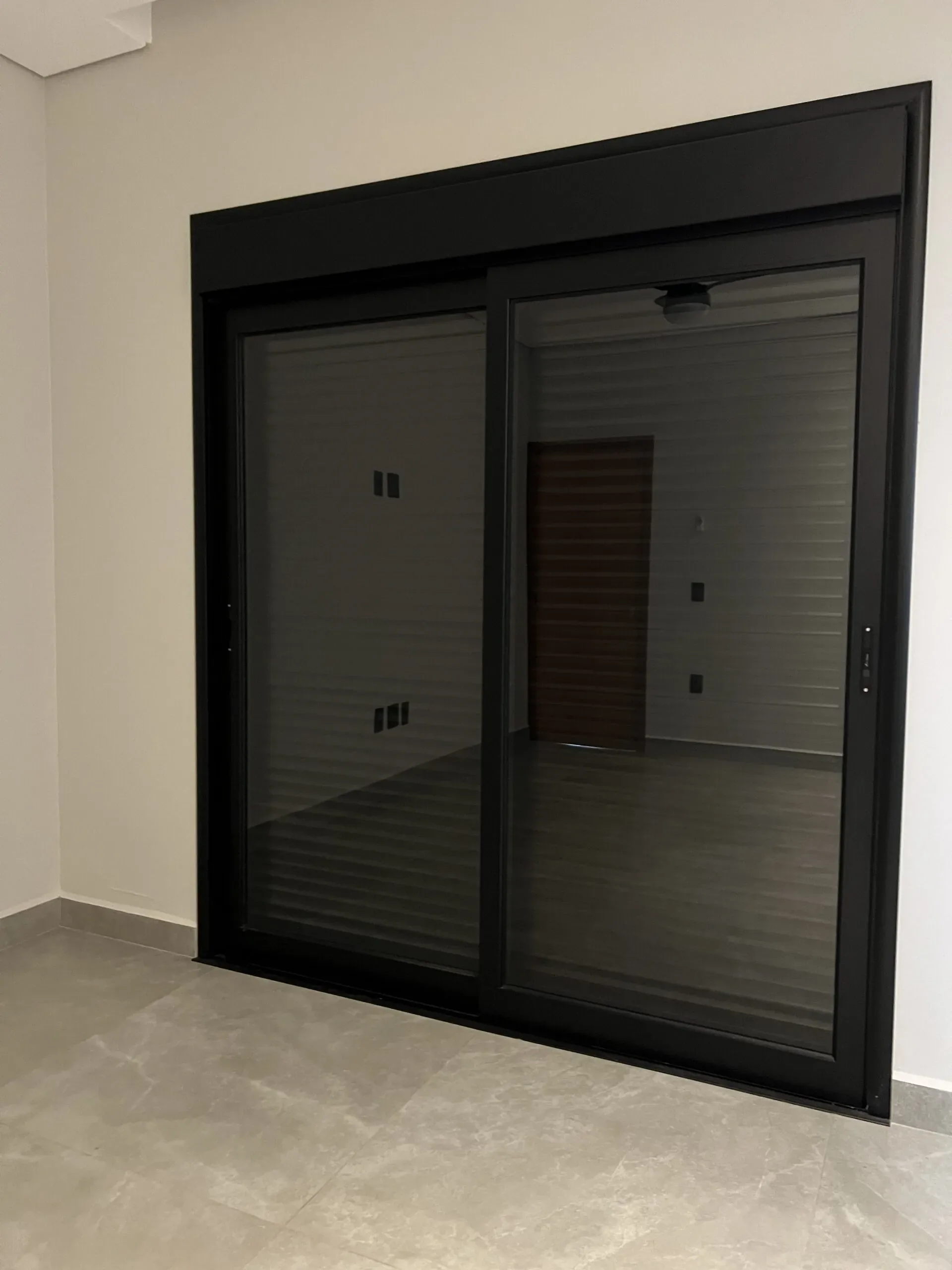 Porta de correr de duas folhas com vidro escurecido e perfil em alumínio preto em ambiente residencial.