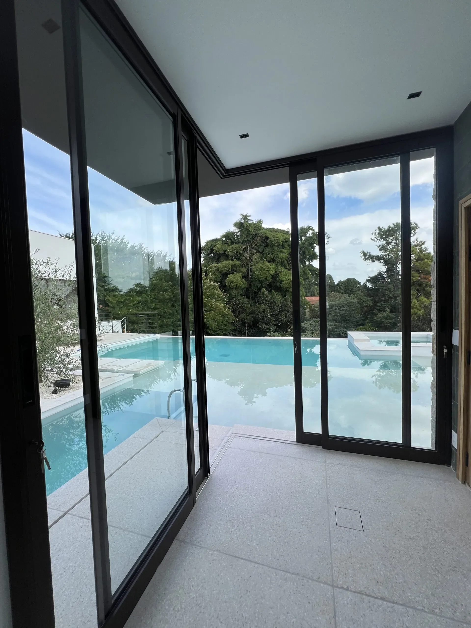 Porta de correr de vidro aberta com vista de dentro para fora para piscina e área verde