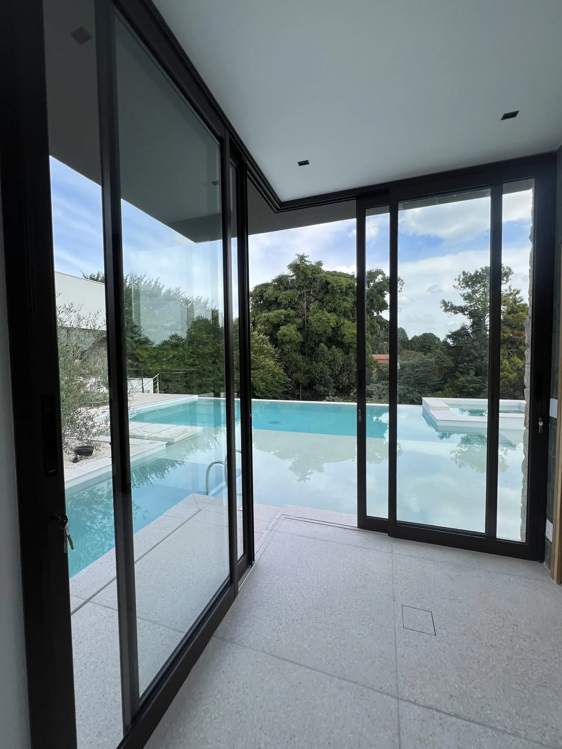 Vista interna através de portas de correr de vidro com esquadrias escuras voltadas para área de piscina e jardim