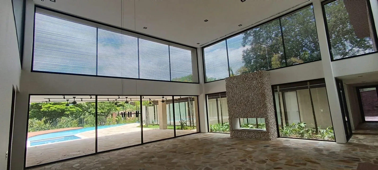 Sala de pé-direito duplo com portas de correr de vidro e janelas de alumínio com persianas integradas