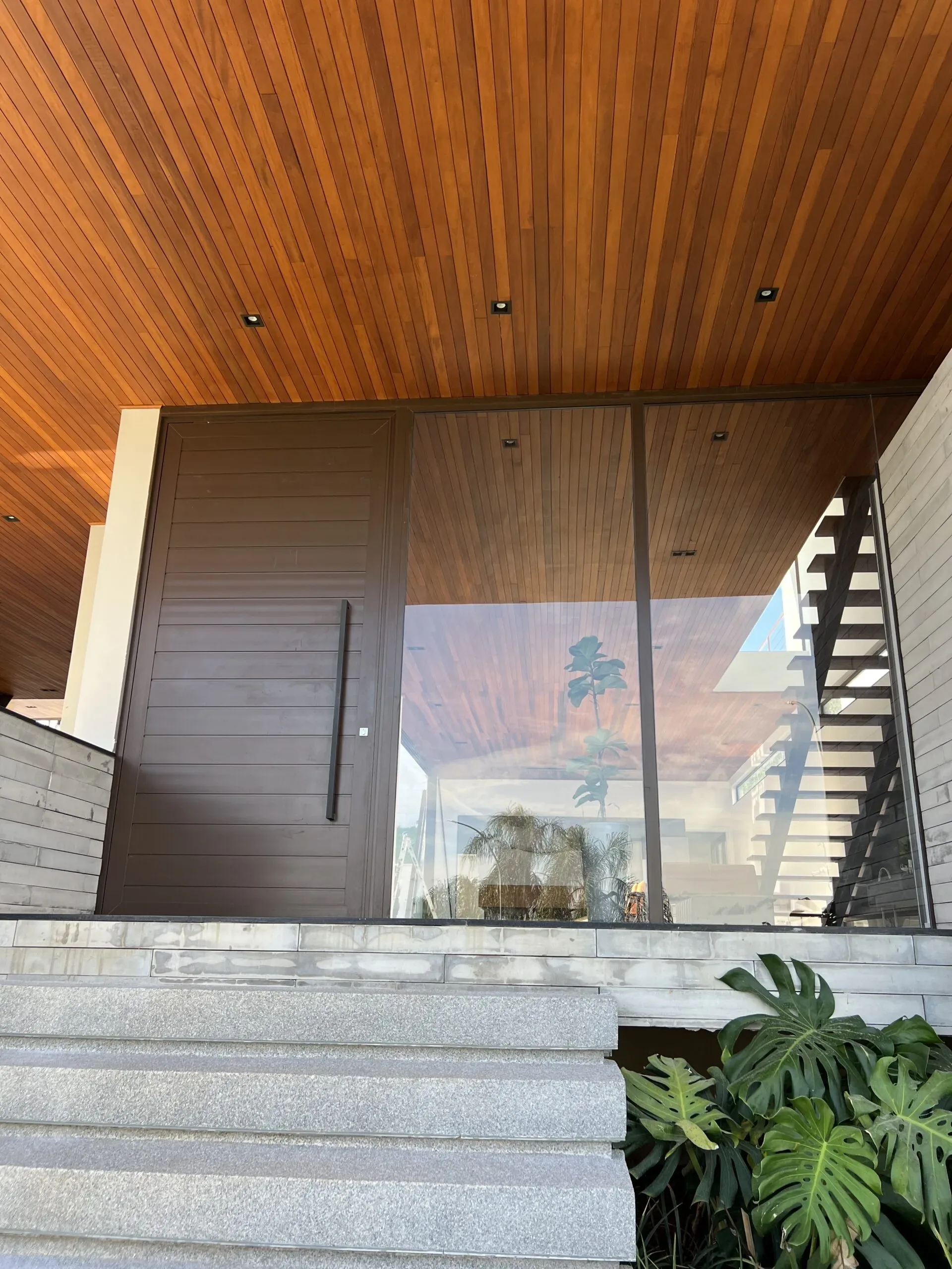 Fachada de alto padrão com porta pivotante em alumínio marrom