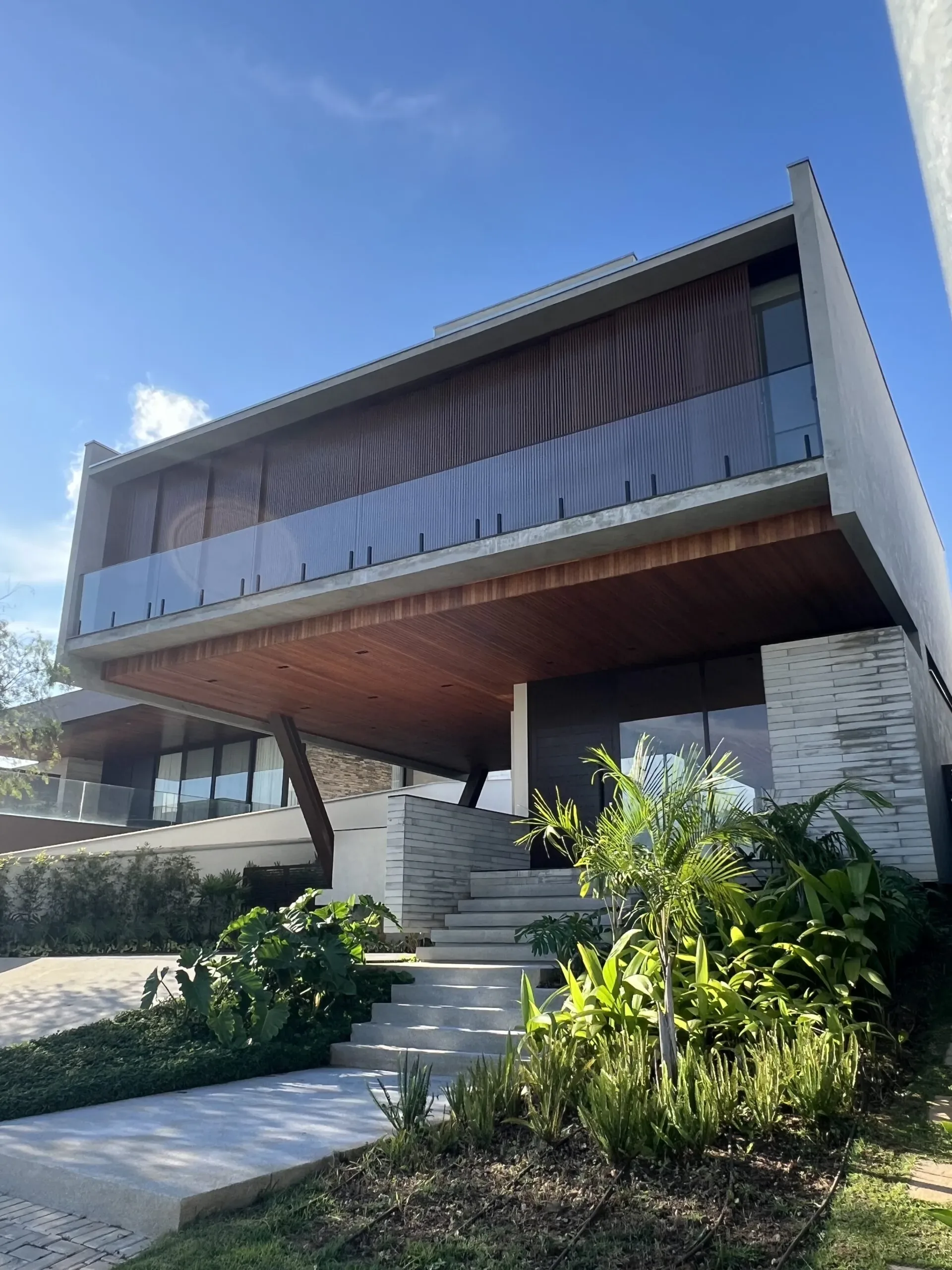 Casa moderna com fachada imponente, destacando balanço em concreto, brises no pavimento superior e grandes aberturas em vidro