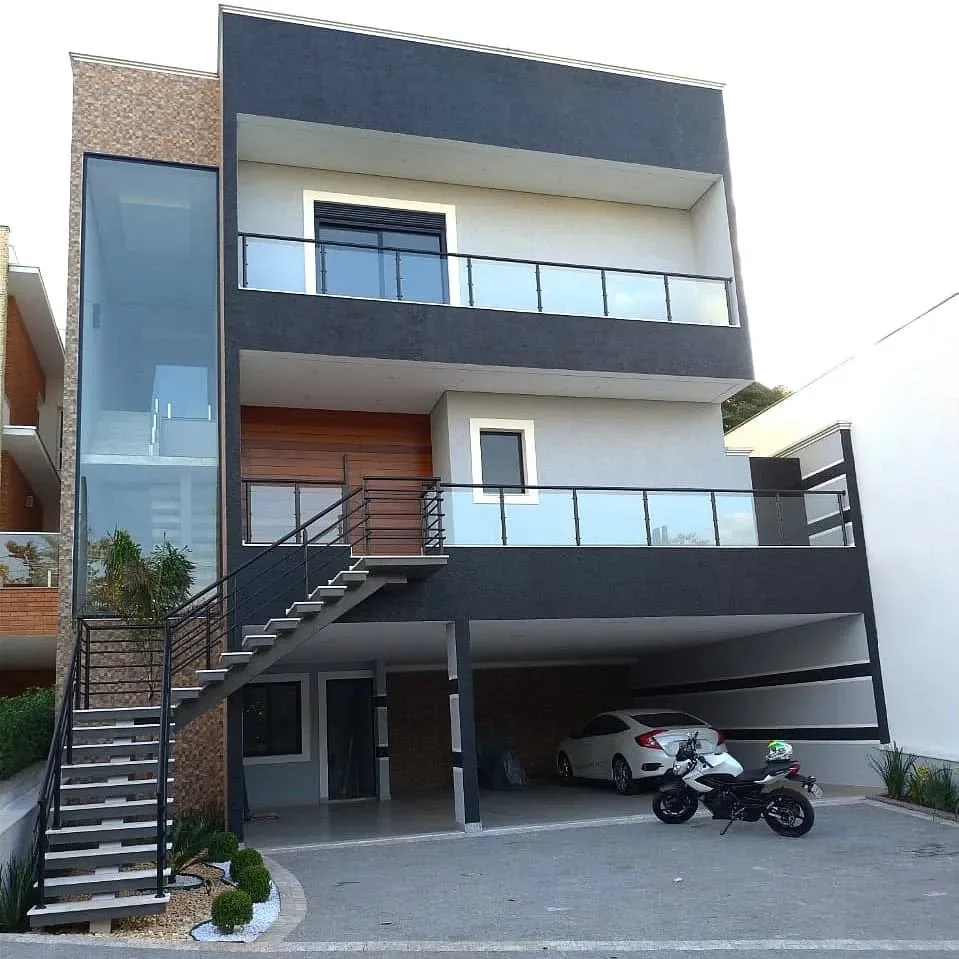 Fachada frontal de sobrado moderno de três pavimentos com guarda-corpo em alumínio preto e vidro temperado nas sacadas e escada helicoidal externa.