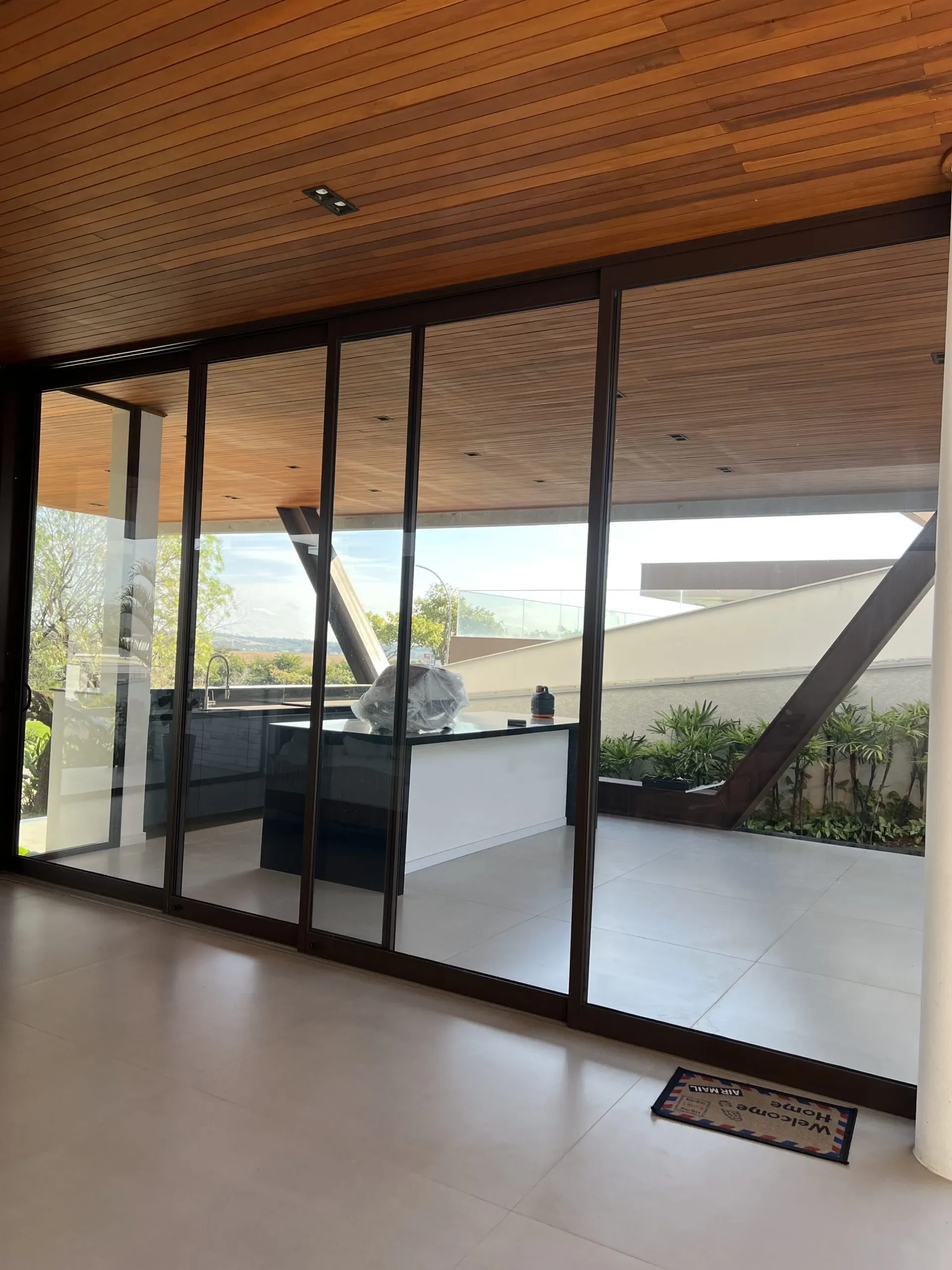 Sistema de portas de correr de vidro com esquadrias escuras integrando ambientes, com vista para área de lazer sob cobertura de madeira