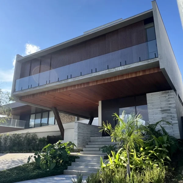 Casa moderna com fachada imponente, destacando balanço em concreto, brises no pavimento superior e grandes aberturas em vidro.